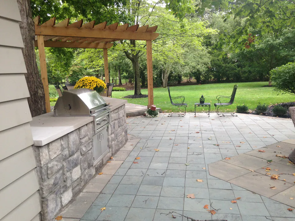 Stone grill counter under a cedar pergola on a bluestone patio overlooking a lawn